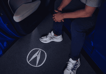 Person stepping out of 2026 Acura Integra with Acura logo projected on the ground