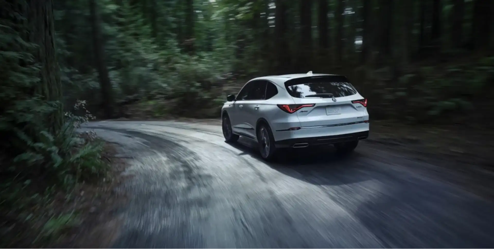 Rear view of the 2026 Acura MDX driving through a wooded road
