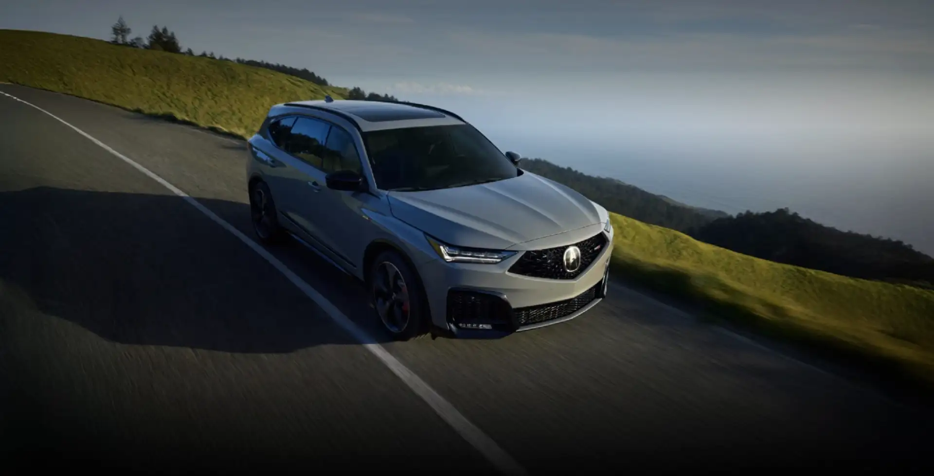 Acura MDX Type S SUV drives along a winding coastal road with grassy hillsides