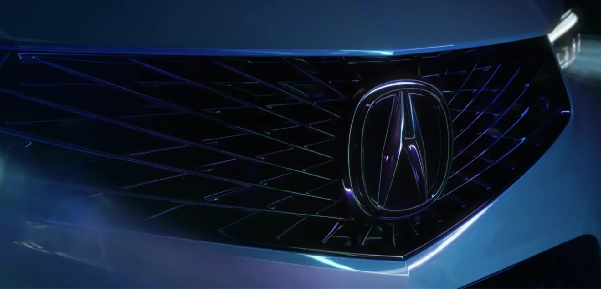 Close-up of an Acura grille and emblem lit in deep blue light