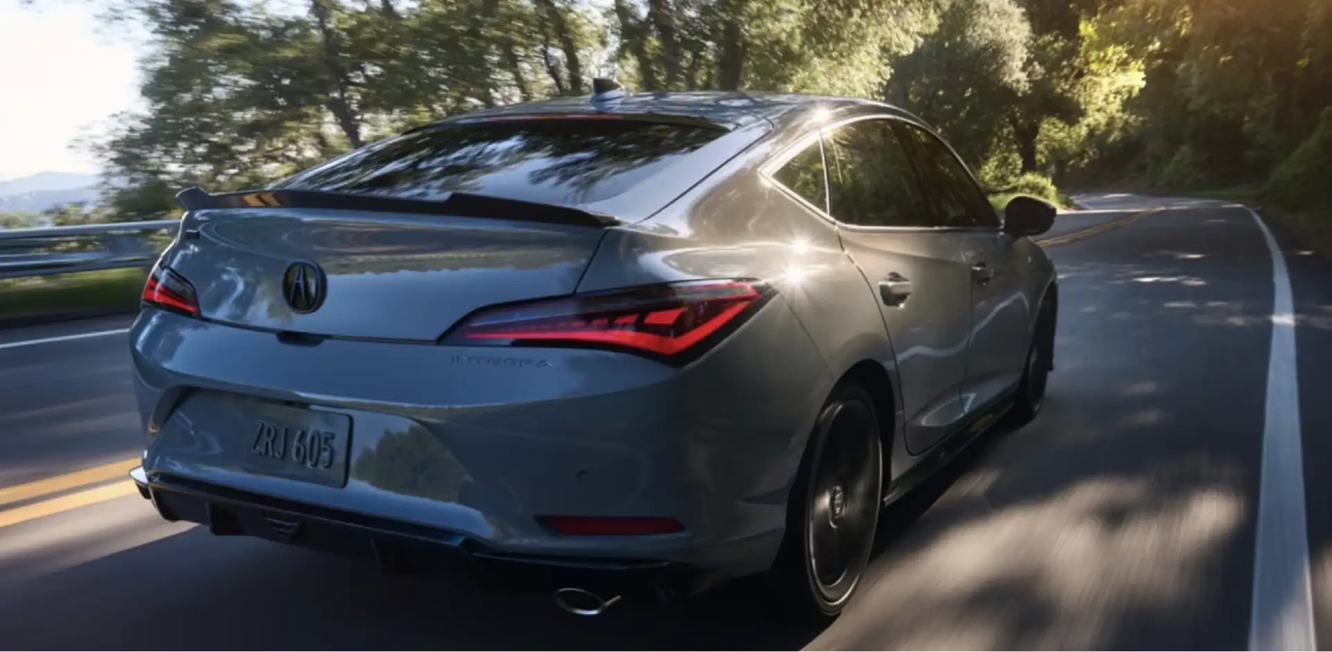 Rear view of an Acura Integra driving down a sunny, tree-lined road