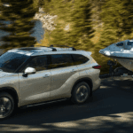 White 2020 Toyota Highlander towing boat through wooded lake highway