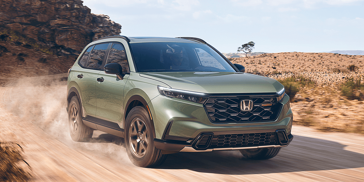 2026 honda cr-v in ash green metallic traveling down a dirt road in the desert during the day`