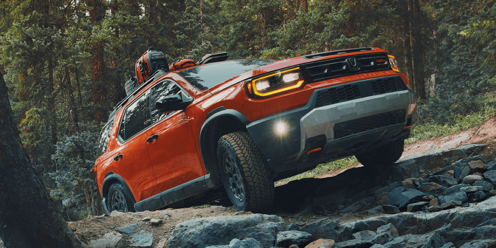 2026 honda passport in sunset orange driving over rock with a dense forest backdrop and cargo on the roof