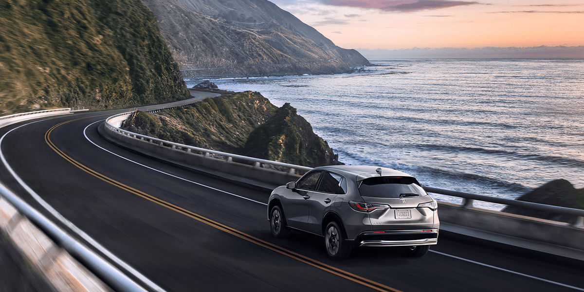 2026 honda hr-v in modern steel driving away from viewer on a coastal highway at sunrise