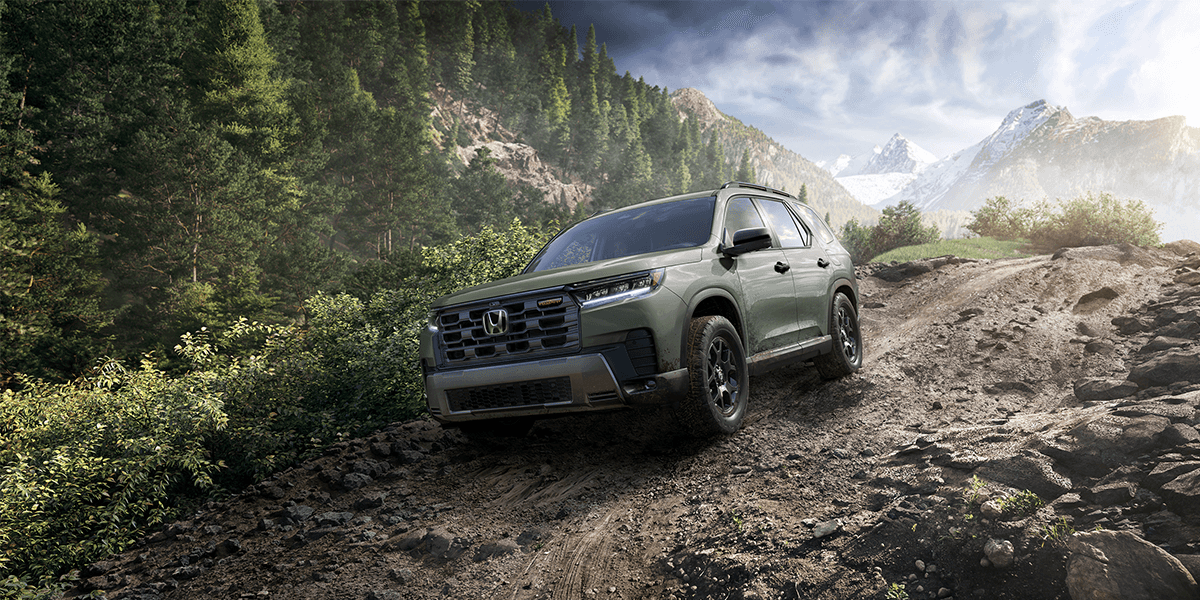 2026 honda pilot in ash green metallic driving down a dirt road with a mountain backdrop