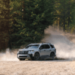 2026 honda pilot in solar silver metallic driving on a dirt road with a forest backdrop and dirt kicking up behind the suv