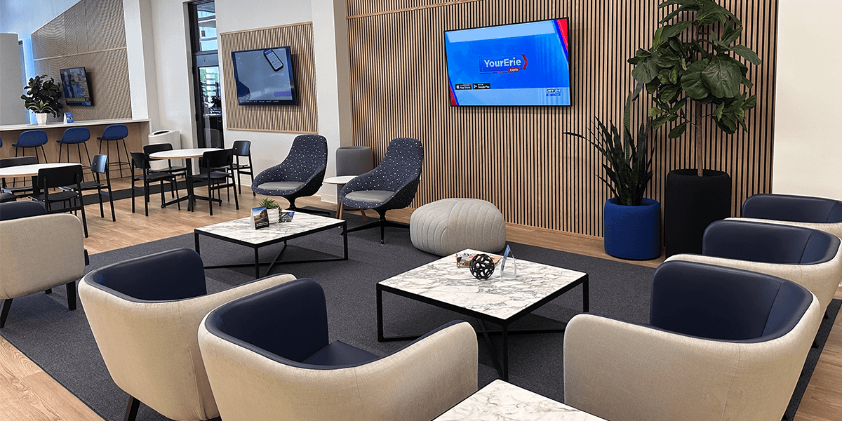 bianchi honda customer lounge with soft vinyl chairs, marble coffee table, blue carpeting, and tv on walls with plants and miscellaneous decor
