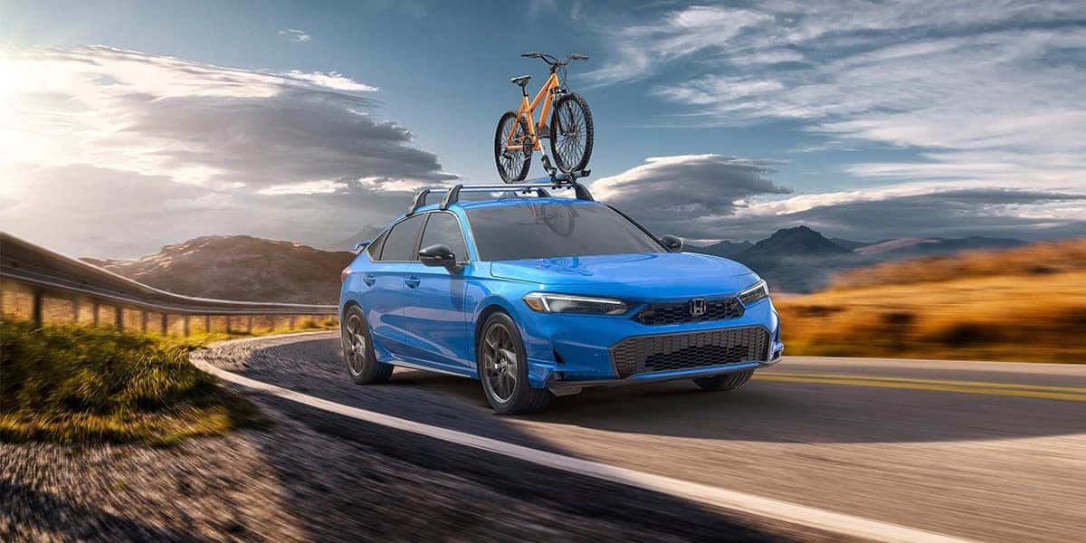 2026 honda civic hatchback in boost blue pearl with an orange bike on roof rack driving in a mountain/field landscape