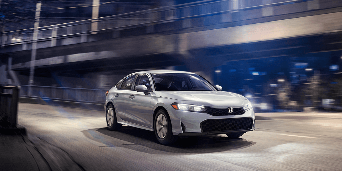 2026 honda civic sedan in solar silver driving fast through a city scape at night