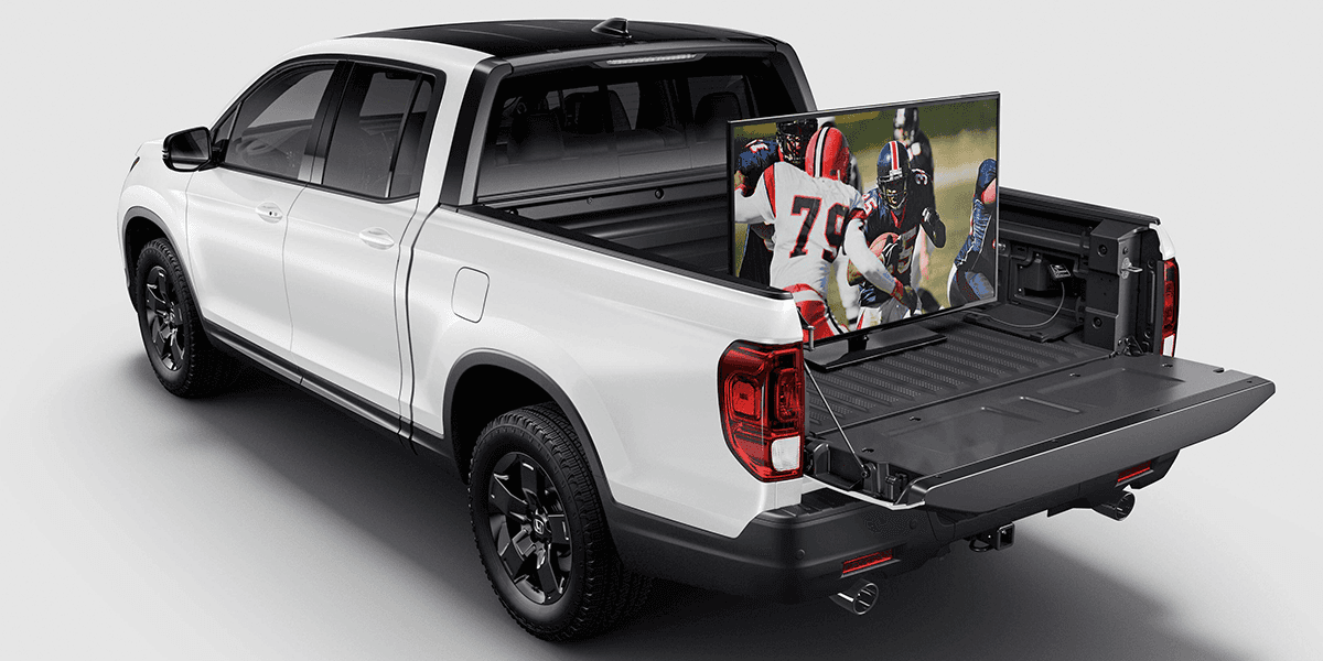 white honda ridgeline on white background with a tv in the tailgate screening a football game