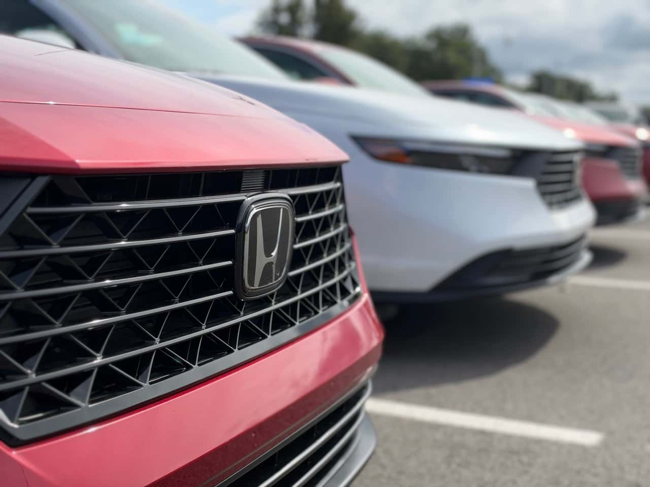 Honda emblem on the front of a red honda accord with other cars in the background