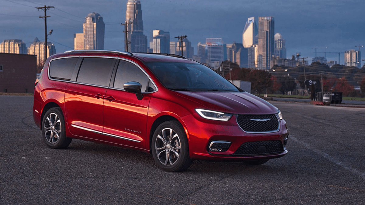 A red Chrysler Pacifica in a parking lot with a city in the background.