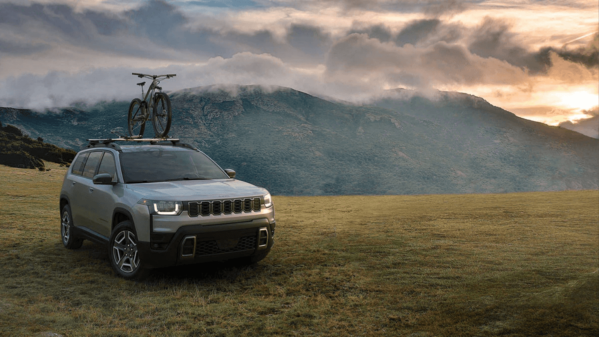 A gray Jeep Cherokee on a field with a bike attached to the top.