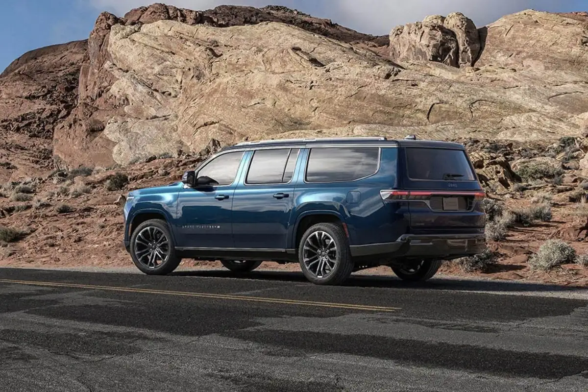 A blue Jeep Grand Wagoneer pulled off the side of the road by rocky hills