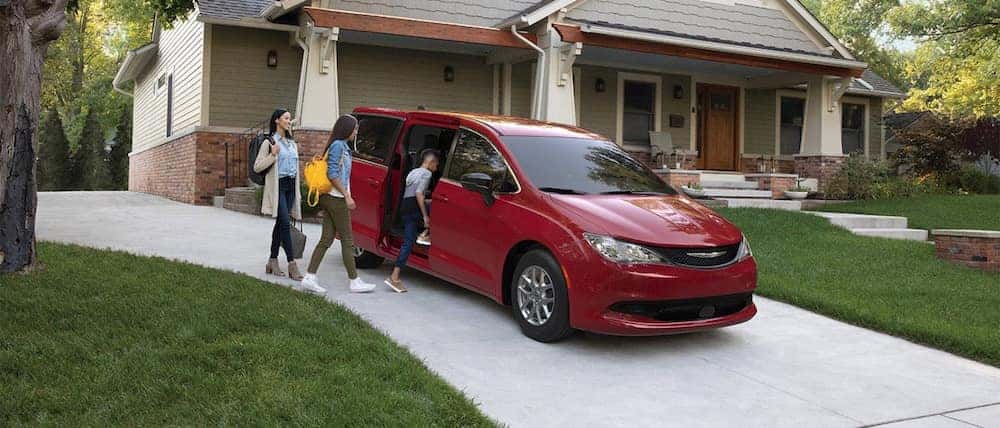 A family getting into a red 2026 Chrysler Voyager minivan parked in a driveway