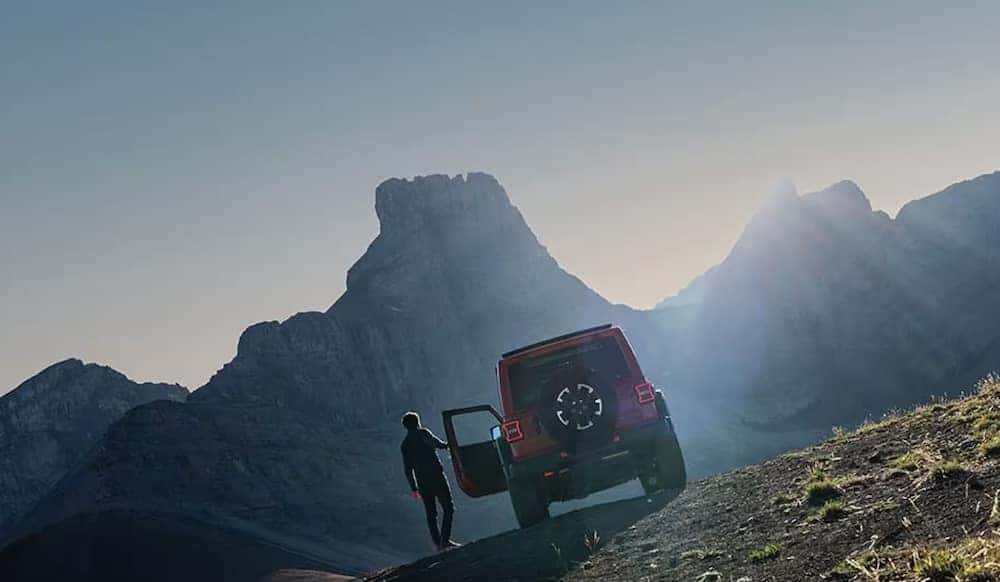 A person getting into a red 2026 Jeep Wrangler parked on a mountain