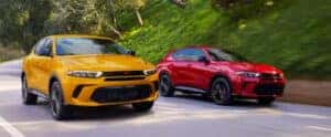 red and yellow 2024 Dodge Hornets driving side by side down a road in a forest area