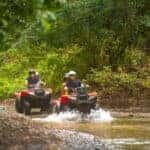 two people riding red ATVs through water of an ATV trail