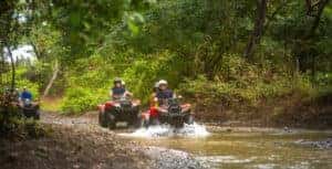 two people riding red ATVs through water of an ATV trail