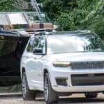 white 2024 jeep grand cherokee towing a boat down a forested road