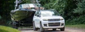white 2024 jeep grand cherokee towing a boat down a forested road
