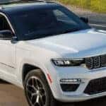 white 2024 jeep grand cherokee 4xe driving down a road