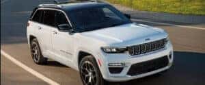 white 2024 jeep grand cherokee 4xe driving down a road