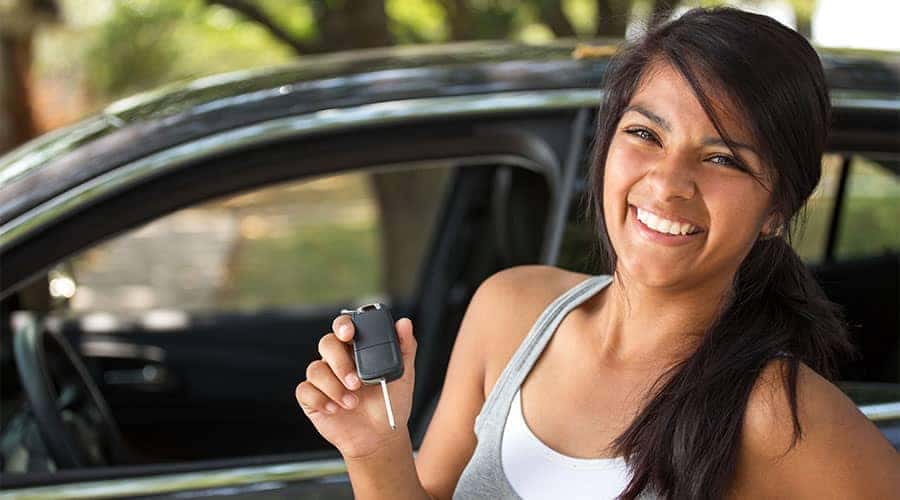 Woman holding key in front of new car