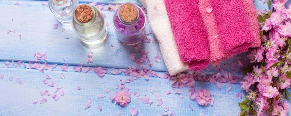 A few bottles of essential oil next to a towel, with flower petals strewn about.