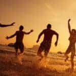 Four friends running into the waves on a beach
