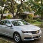 A silver Chevrolet Impala sedan parked on a scenic, tree-lined suburban street with soft, natural light.