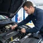A professional mechanic is shown working on a Chevrolet engine in a clean service bay.