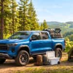 A modern Chevy Colorado truck parked next to a camping tent at a sunny wilderness campsite.