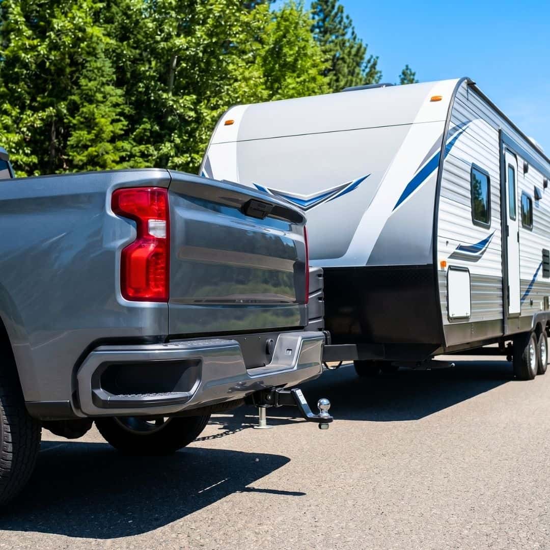 Close-up of a Chevrolet truck hitched to a travel trailer on a sunny day.