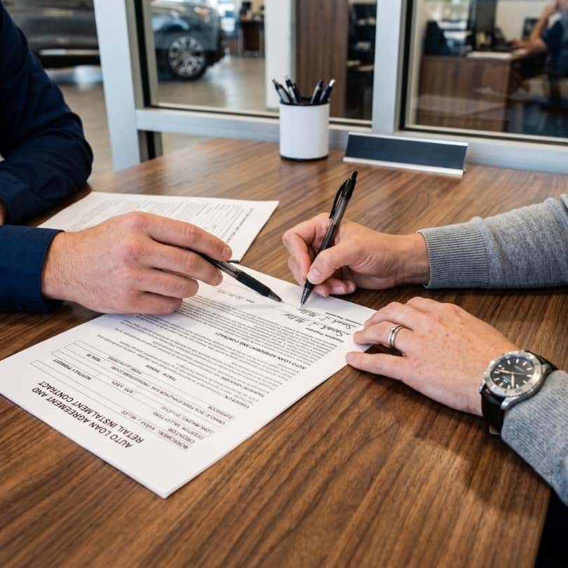 A close-up of hands signing an auto loan contract.