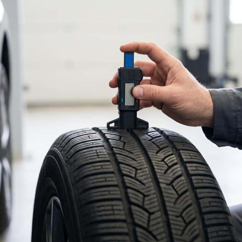 A technician uses a digital gauge to check the tire tread depth on a car.