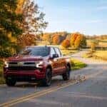 A Chevrolet Silverado pickup truck drives down a tree-lined rural road