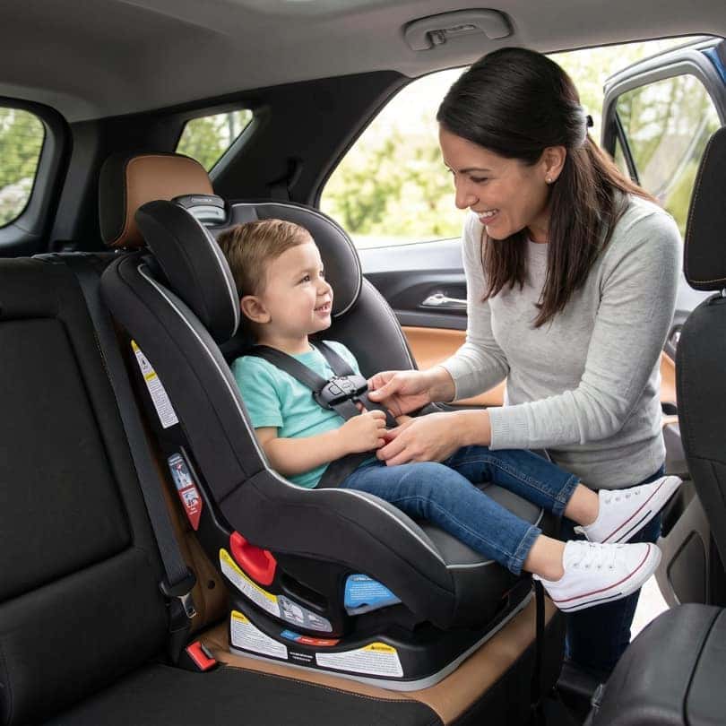 A mother buckling a young child into a car seat in the back of a Chevrolet Equinox.
