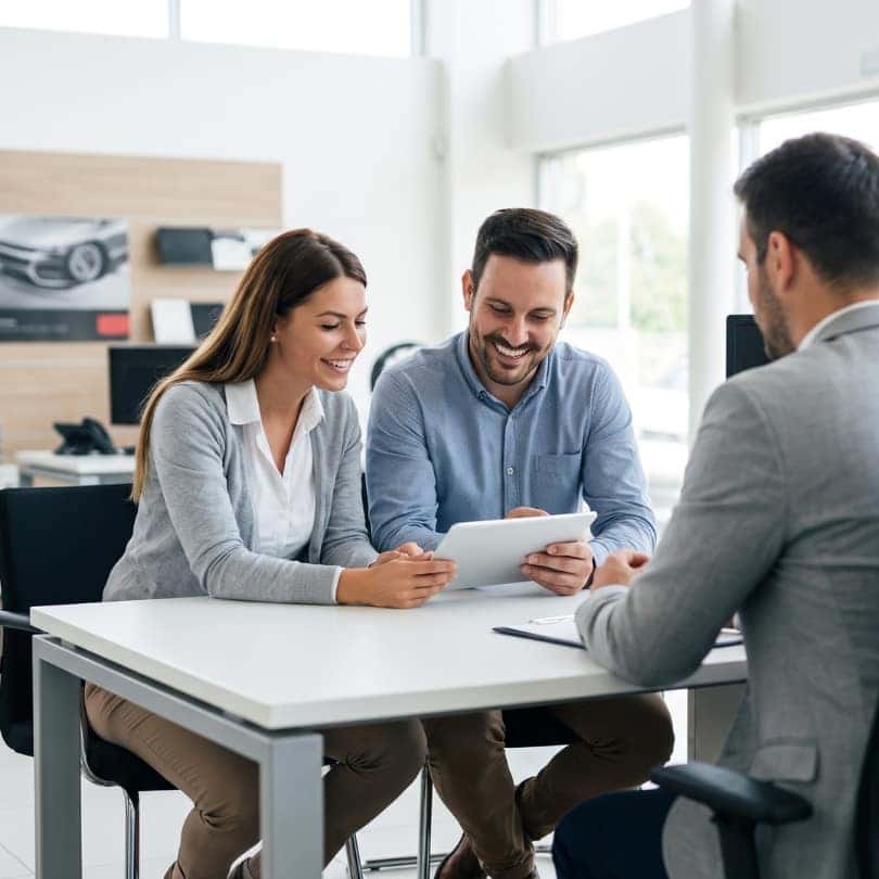 A happy couple meeting a salesperson at a car dealership.