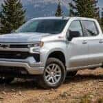 A silver Chevrolet Silverado Z71 pickup truck navigates a rugged dirt trail with a scenic mountain backdrop under natural light.