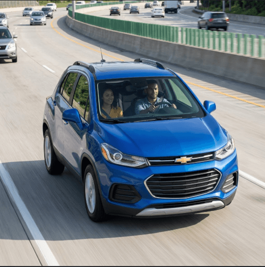 Confident driver in a modern blue Chevrolet Trax smoothly accelerates onto a busy highway during a bright day.