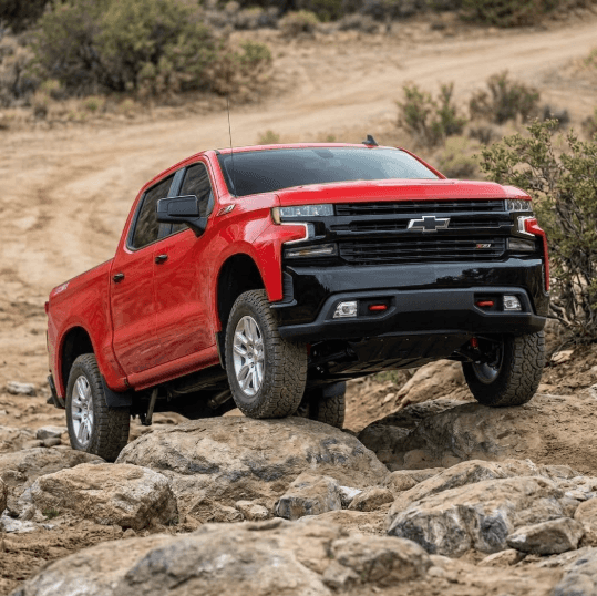 A red Z71 Silverado truck actively drives over rough rocks, demonstrating the essential protection provided by its dark underbody skid plates.