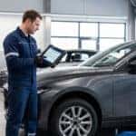 A technician with a tablet inspects a modern sedan in a bright service bay.