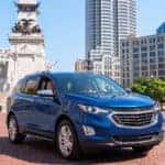 A smiling couple driving a blue SUV past the Soldiers and Sailors Monument in downtown Indianapolis.