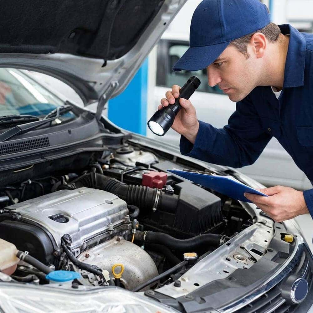 An inspector checking a used car engine with a flashlight and clipboard.