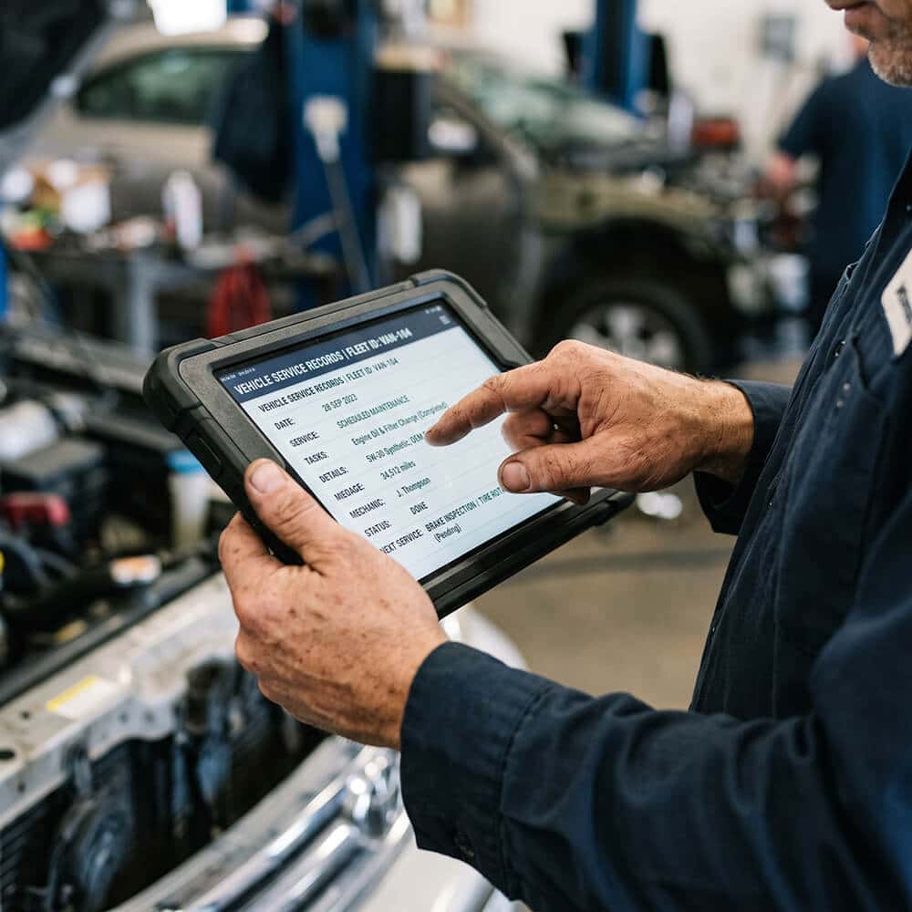 A detail shot of hands using a tablet to review vehicle maintenance data.