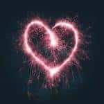 Pink sparklers at night being waved around in the shape of a heart.