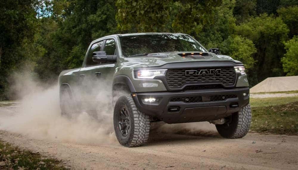 An olive green 2026 Ram pickup driving down a dusty road
