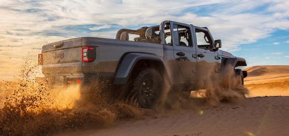 A gray 2026 Jeep Gladiator truck driving over a sand dune